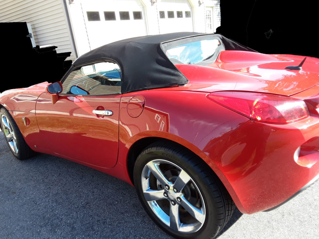 Side view of 2008 red and black Pontiac Solstice with top up.