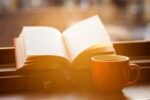 Open book propped on windowsill with coffee cup